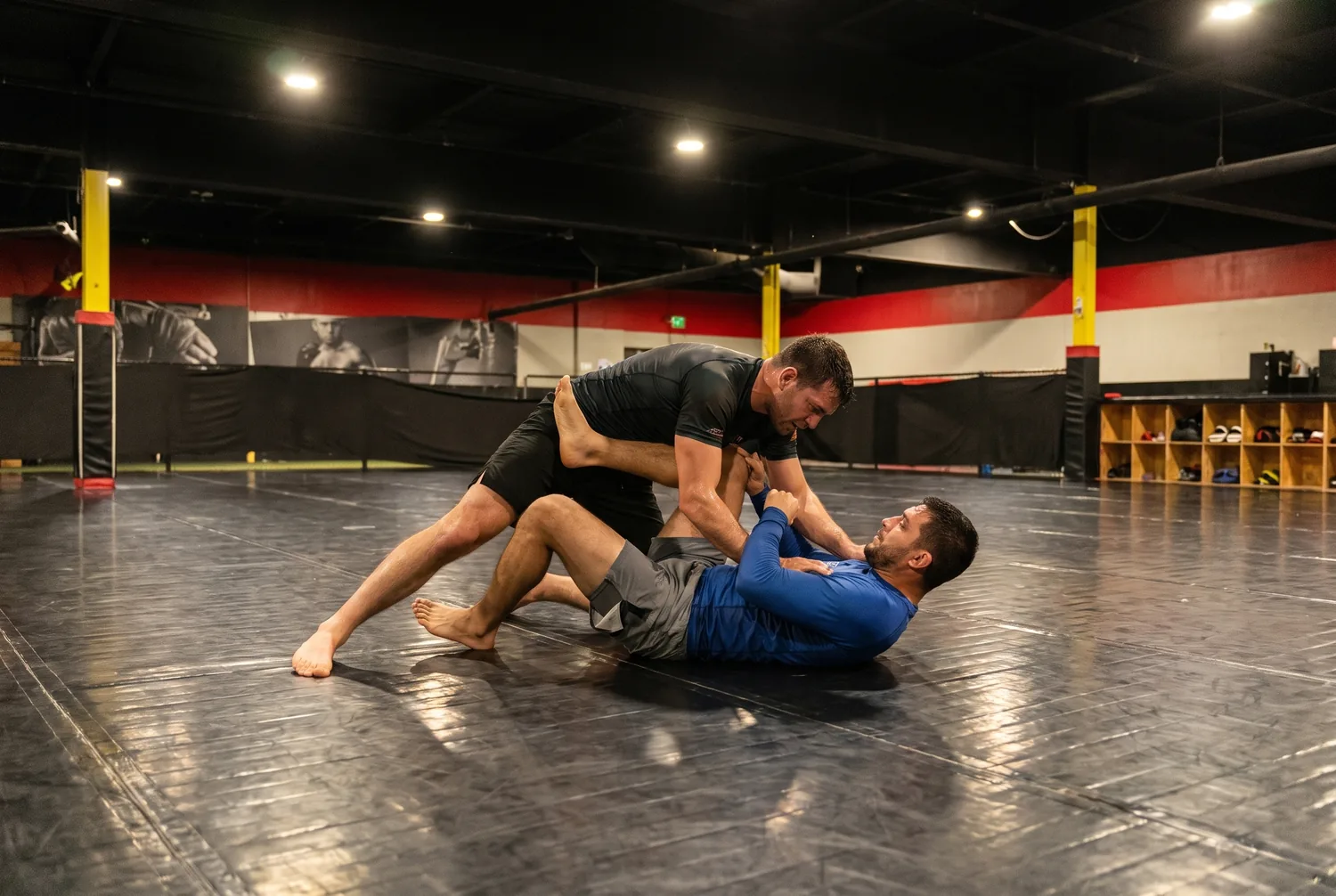 Two adult Brazilian Jiu-Jitsu students grappling on the black mats at Xtreme Couture