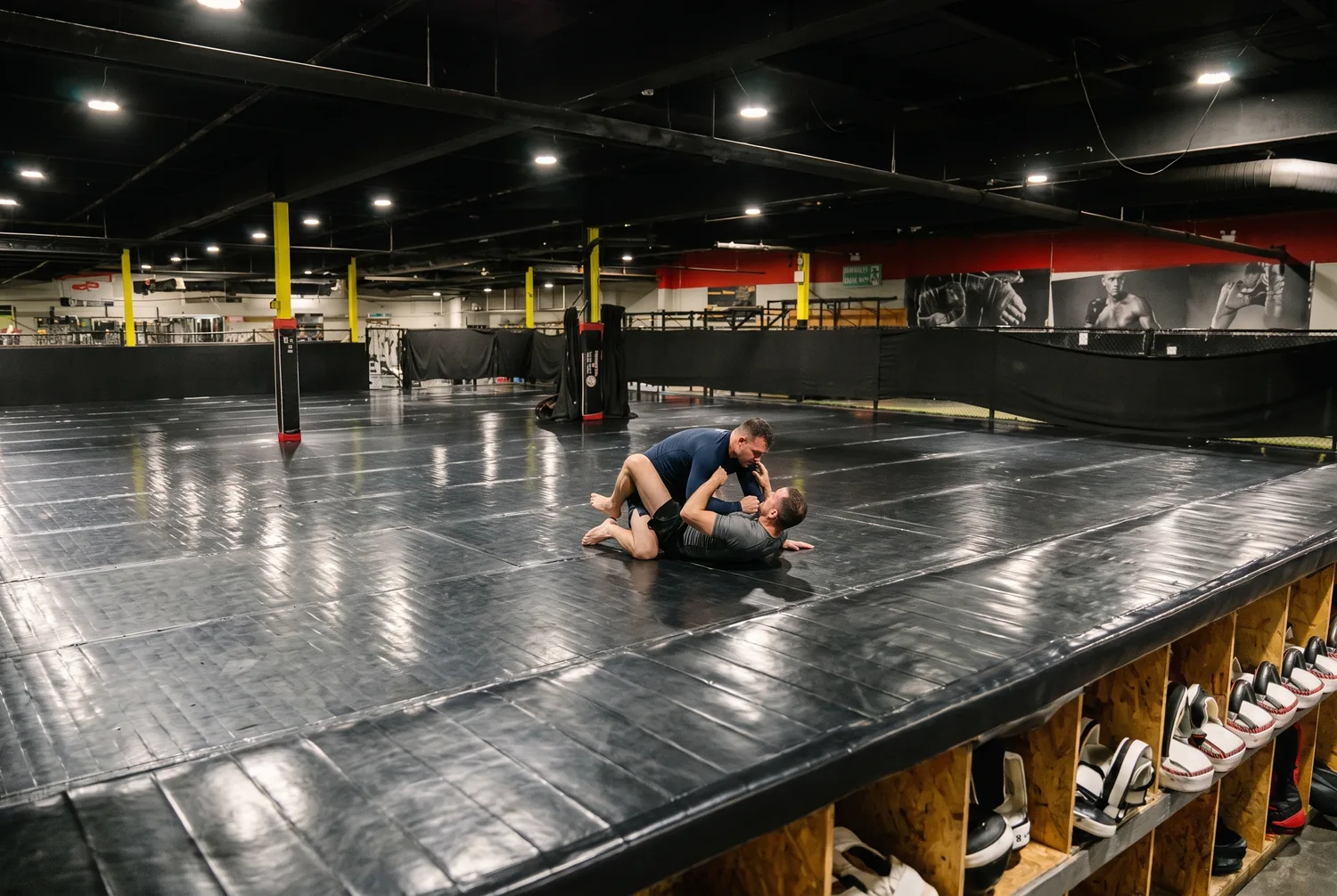 An adult grappler establishing top control over a training partner on the black mats